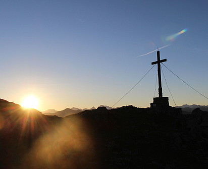 ein Gipfelkreuz mit einem Sonnenuntergang als Hintergrund beim Sporthotel Sillian 